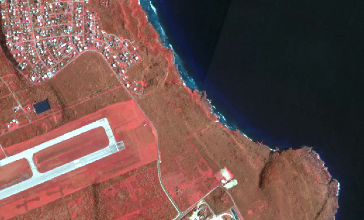 Planet SkySat color infrared image of southern Saipan following Typhoon Sinlaku in April 2026, with healthy vegetation in bright red, the island's international airport at center right, and the reef along the western coast