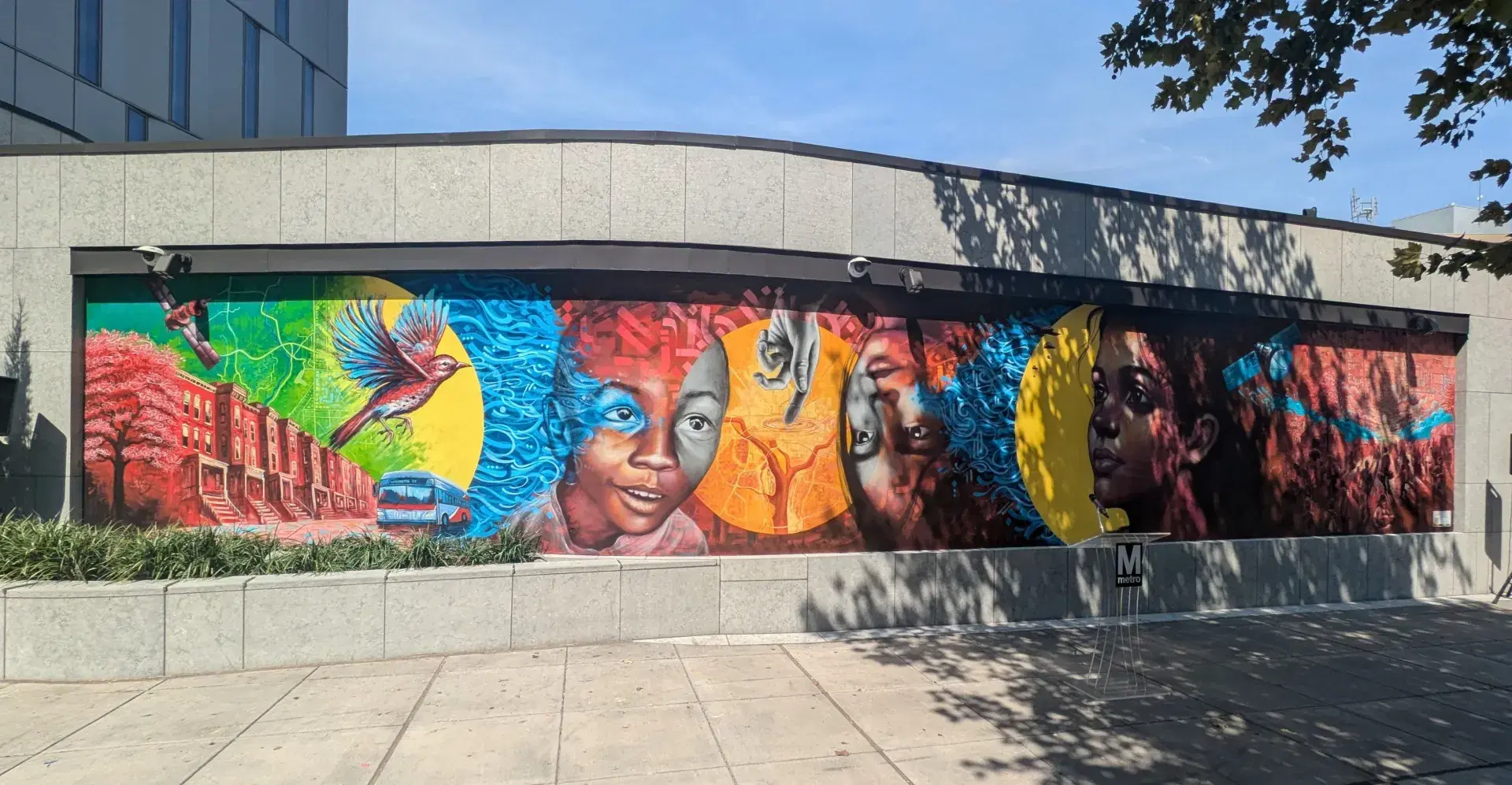 A brightly colored NASA Lifelines mural depicting a satellite, a city street and metro bus, a bird in flight, children pointing at a map of Washington, D.C., and a group of people working together under a satellite map