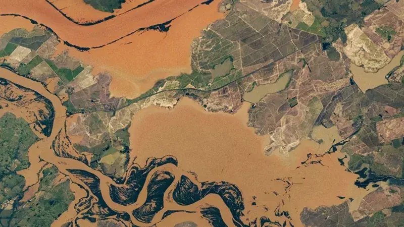 Satellite view of a flooded river system carrying heavy sediment across farmland and wetlands