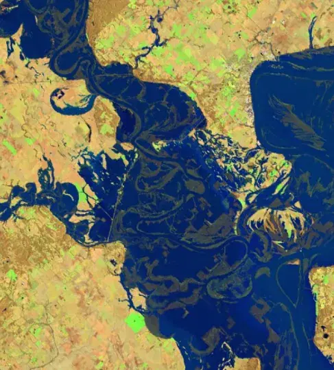 False-color satellite view of a flooded river system, with standing water in dark blue against tan terrain and green vegetation.