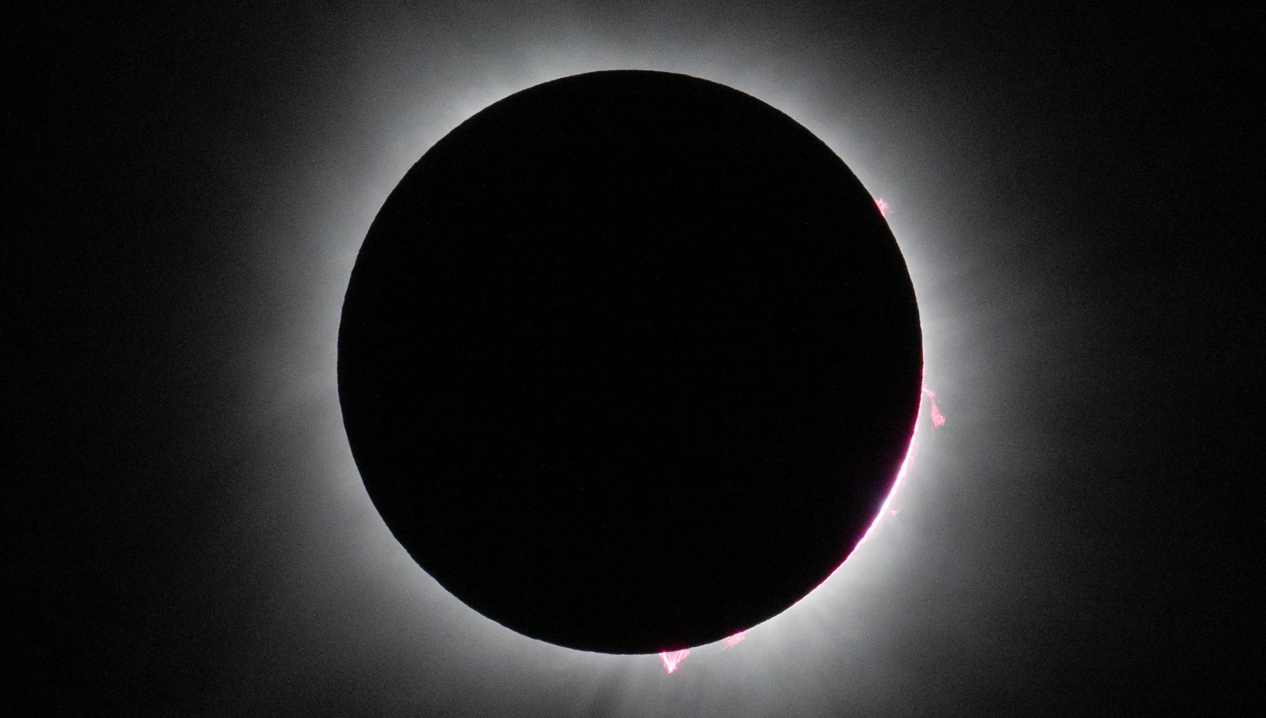 The 2024 total solar eclipse with pink solar prominences visible on the edge of the disk.